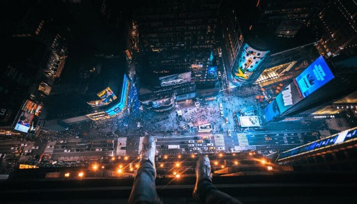 high-angle photo shows a person's legs dangling over the edge of a tall building symbolizing the risk and feeling of being dangerously exposed that can come with trying to sell a home FSBO (For Sale By Owner)